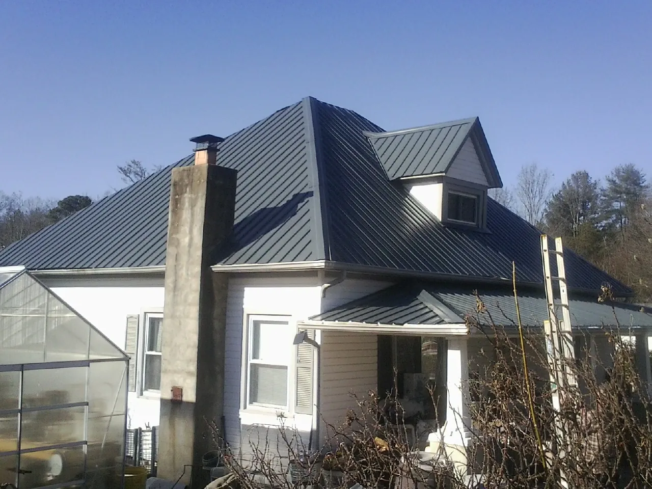 Dark blue standing seam metal roof on a white farmhouse with dormer — Slate & Tile Roof Repair by Roofing Brothers in Hungry Horse
