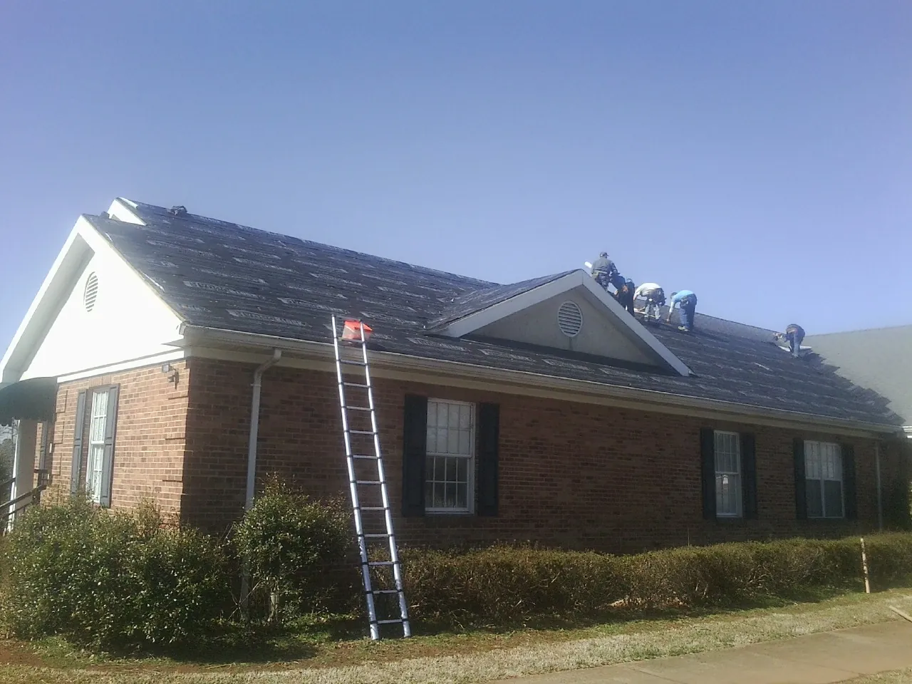 Crew tearing shingles off a brick ranch roof with a ladder set — Metal Roof Repair work by our crew in Hungry Horse