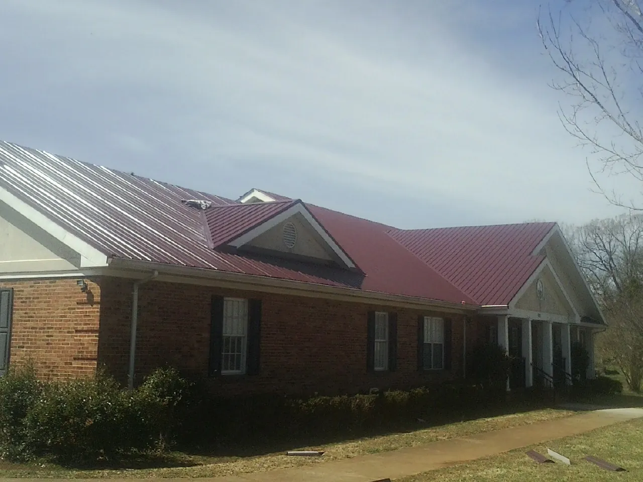 Red metal roof with gabled entries on a long brick building, from a Hail Damage Roof Repair job in Hungry Horse