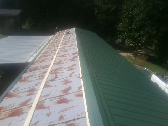 Old rusted panels beside newly installed green metal roofing — Wind Damage Roof Repair by Roofing Brothers in Hungry Horse