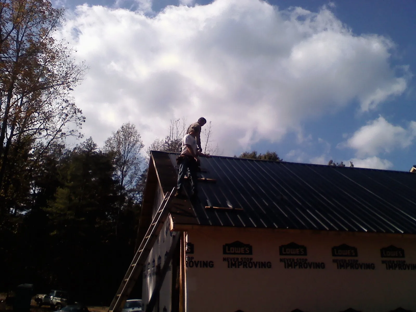 Roofer fastening dark metal panels high against a cloudy sky, from a Roof Inspection job in Hungry Horse