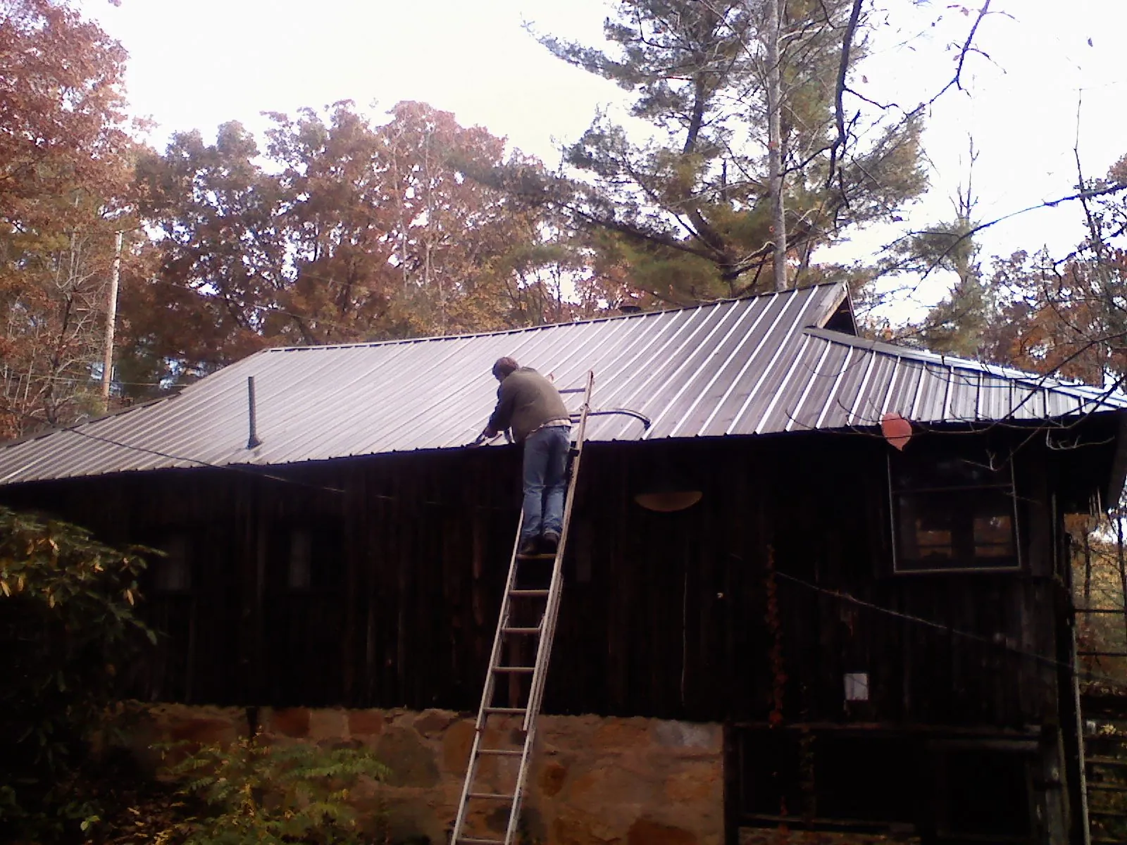 Roofer on a ladder working along the edge of a cabin metal roof in Hungry Horse