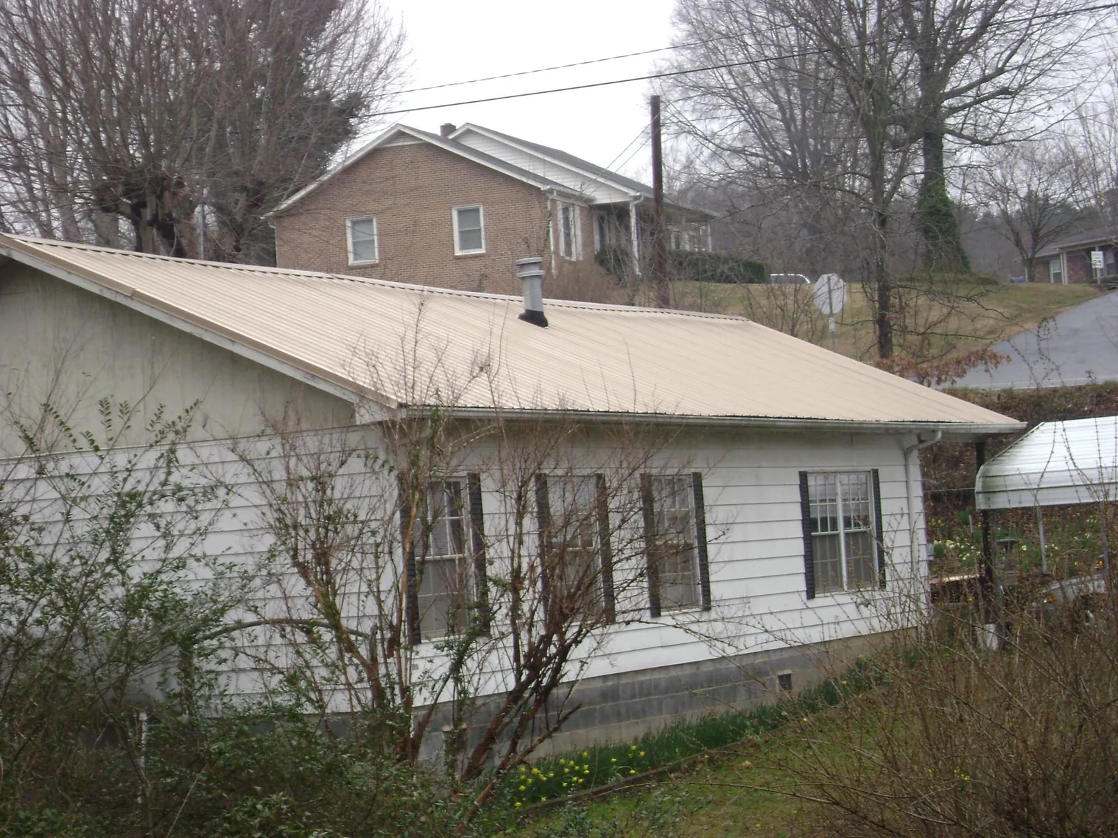 Tan metal roof on a white sided house set into a hillside — Commercial Roofing by Roofing Brothers in Hungry Horse